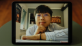 Nominierter Hao Yu. Junge, asiatisch und männlich gelesene Person mit schwarzen Haaren sitzt am Schreibtisch und stützt sein Kinn auf seine rechte Hand. Er trägt eine silberne Brille und ein blau-weiß gestreiftes Hemd.